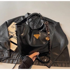 Detail der schwarzen Handtasche aus glänzendem Wachsleder mit goldenem Anhänger