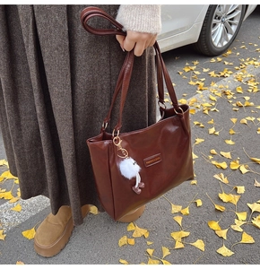 Detail of coffee brown PU leather tote bag with plush charm on a leaf-covered street