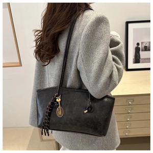 Detail of black tote bag with braided tassel and golden tennis racket charm on shoulder