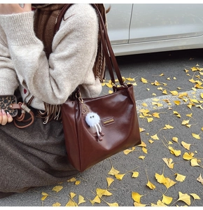 Detail of dark brown leather tote bag with a white plush charm on a model's shoulder
