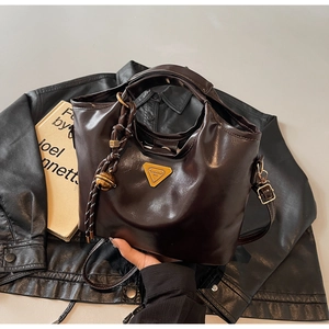 Details einer dunkelbraunen Handtasche mit Dreieckslogo und geflochtenem Anhänger auf Jacke