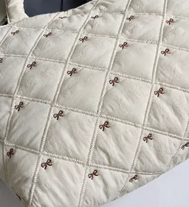 Détail du sac fourre-tout matelassé crème avec broderie nœud marron et tissu ultra léger