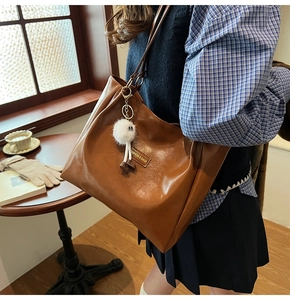 Brown vintage faux leather tote bag with furry charm and side logo in a cafe setting