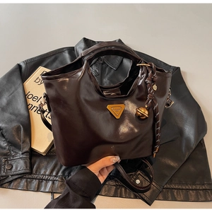 Detail einer dunkelbraunen Lederhandtasche mit goldenem Logo und geflochtenem Anhänger