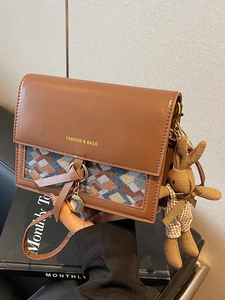 Brown crossbody bag with knit pattern and rabbit charm in warm studio setting