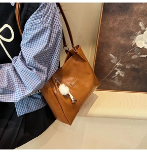 Close-up of brown leather tote bag with a white fluffy pompom charm and fashion logo
