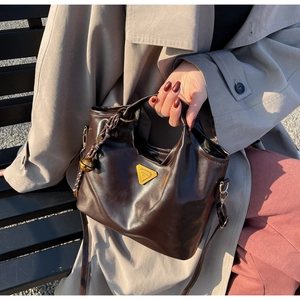 Detail einer dunkelbraunen Ledertasche mit goldener Hardware und geflochtenem Anhänger