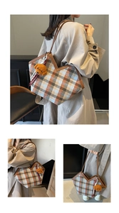 Detail of plaid tote bag featuring brown leather straps and a plush bear pendant charm