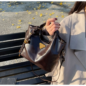 Detailansicht der dunkelbraunen Lederhandtasche mit goldenem Logo und Quasten-Akzent