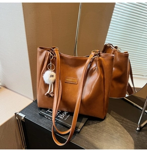 Brown leather tote bag with FASHION & BAGS tag and white fluffy eye-shaped charm