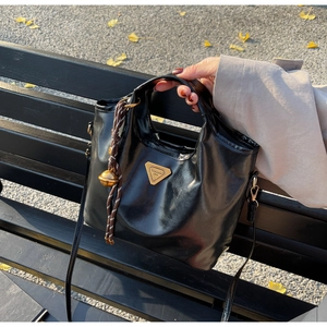 Detailansicht der glänzenden schwarzen Vintage-Handtasche mit goldenem Dreieckslogo aus Metall