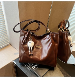 Detail of dark brown faux leather tote bag with FASHION & BAGS label and plush pendant