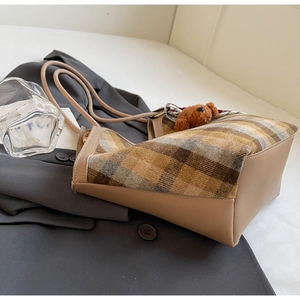 Detail view of retro plaid tote bag with plush bear charm on grey blazer backdrop