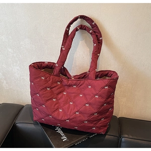 Close-up of quilted burgundy tote bag with white bow embroidery and padded nylon texture