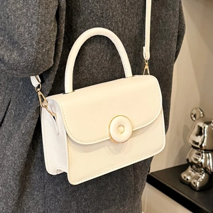 Elegant white structured crossbody bag with gold-trimmed button and top handle