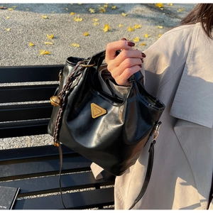 Detail der schwarzen Ledertasche mit goldenem Dreieckslogo und Glockenanhänger-Deko