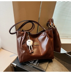 Detail of dark brown faux leather tote bag with glossy finish and plush ball charm