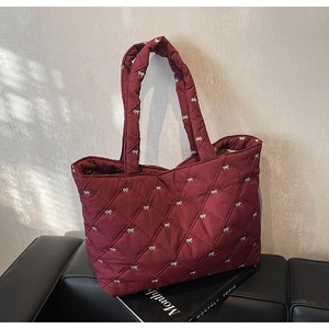 Detail showing burgundy quilted tote bag with white bow embroidery and diamond pattern