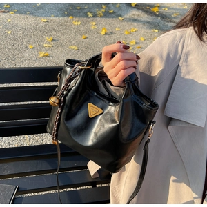 Detail einer schwarzen PU-Ledertasche mit goldenem Logo und dekorativem Glockenanhänger
