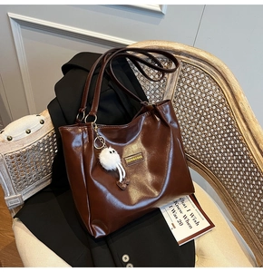 Detail of dark brown glossy leather tote bag with white plush monster charm and fashion logo