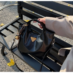 Detailansicht der schwarzen Glanztasche mit goldenem Logo und Glockenanhänger