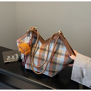 Detail of plaid tote bag with V-shaped opening, brown leather straps and puppy charm