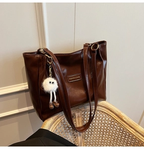 Detail of dark brown tote bag with high-gloss leather and plush monster charm