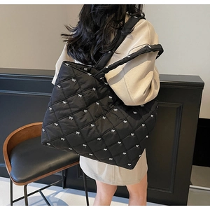 Detail of black quilted tote bag with white bow embroidery and padded shoulder strap