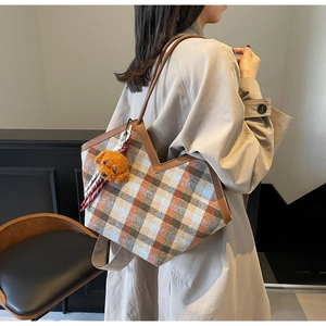 Detail view of plaid tote bag with brown leather handles and teddy bear pendant detail