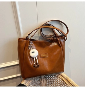 Detail of brown faux leather tote bag with fashion label and white plush toy pendant