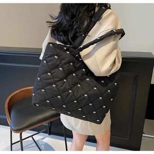 Detail of black quilted tote bag with white bow embroidery shown on shoulder