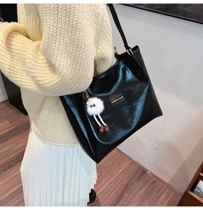 Detail of black glossy leather tote bag with creative plush charm and gold logo plate