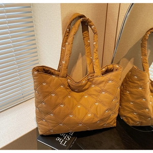 Detail view of caramel brown quilted tote bag with white bow print and wide handles