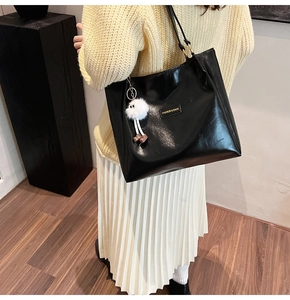 Detail of a black glossy leather tote bag with a golden logo and a white plush charm
