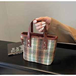 Close-up of vintage plaid wool handbag with brown leather handle and metal rivets
