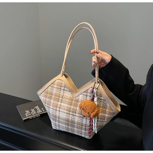 Detail of plaid tote bag featuring checkered wool fabric and brown teddy bear charm