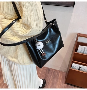 Detail of black leather tote bag with white plush doll charm and fashion label
