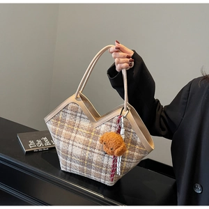 Detail of plaid tote bag with brown leather handles and a plush dog charm pendant
