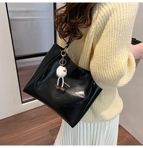 Close-up of black glossy leather tote bag featuring a cute plush doll and fashion tag