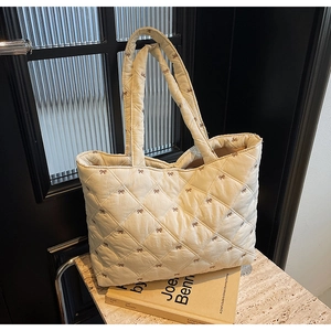 Detail of cream quilted tote bag featuring delicate brown bow embroidery and soft fabric