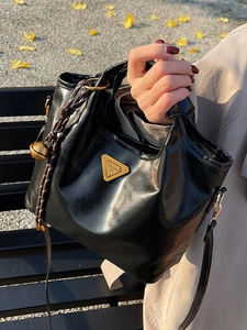 Retro Handtasche aus schwarzem Leder mit goldenem Logo auf Herbstlaub Hintergrund
