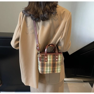 Detail of green plaid wool tote bag featuring brown leather strap and gold metal hardware
