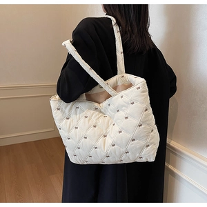 Rear view of a white quilted tote bag with brown bow embroidery worn on a black coat