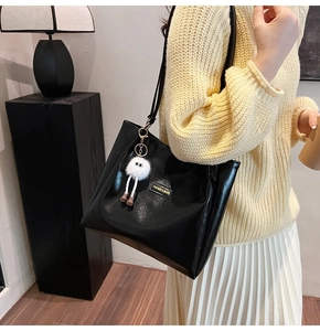Detail of black faux leather tote bag with fluffy monster charm and fashion label