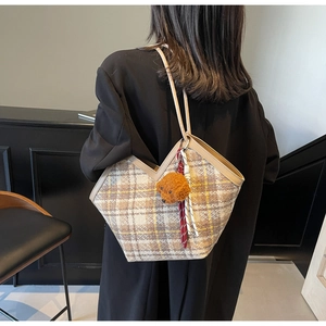 Detail of checkered tweed tote bag with plush puppy pendant shown on model shoulder