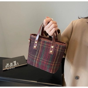 Detail of wool plaid bucket bag featuring leather handles and gold rivet accents