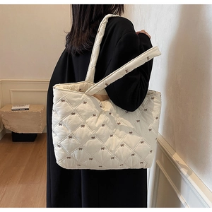 Close-up of beige quilted tote bag with brown bow embroidery and diamond pattern