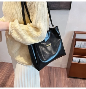 Close-up of black textured tote bag with metal label shown in a cozy lifestyle setting