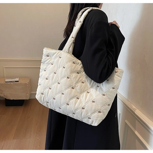 Detail of off-white quilted tote bag with brown bow embroidery and shoulder strap