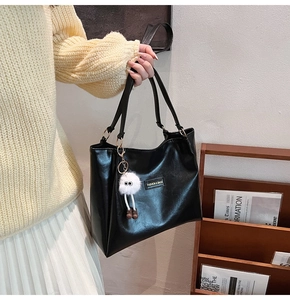 Detail of a black glossy leather tote bag with a white plush doll charm and logo plate